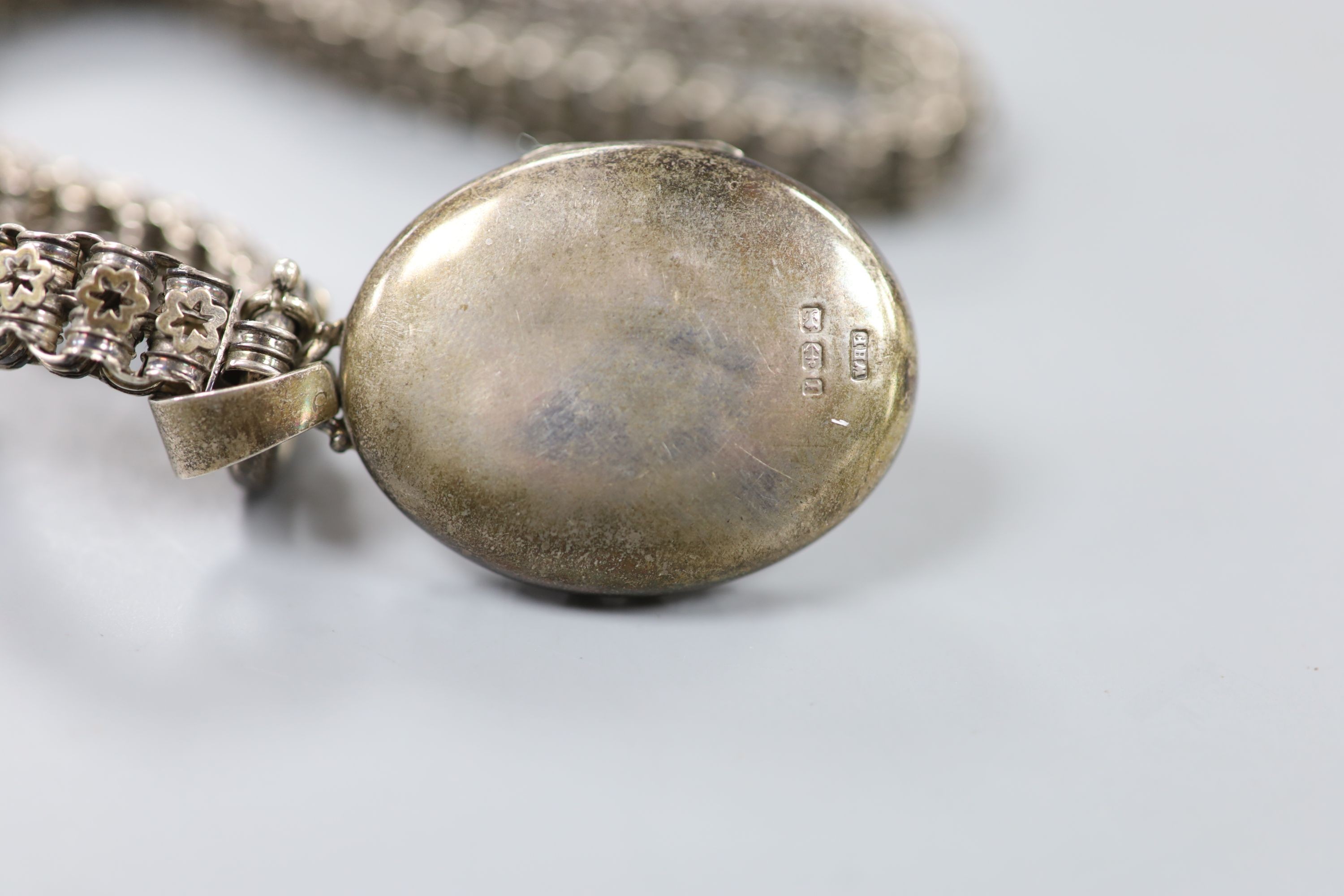 A late Victorian silver oval locket, 45mm, on a pierced white metal chain, 43cm.